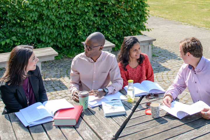 Bild von Studierenden im Freien an Holztisch
