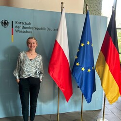 Emilie Funken at the German Embassy in Warsaw next to three flags: Polish, European Union and German