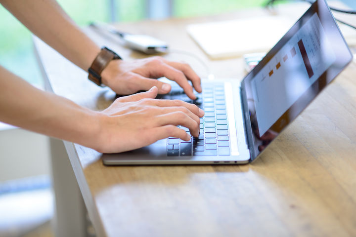Hände einer Person tippen auf einem Laptop auf einem Holztisch.