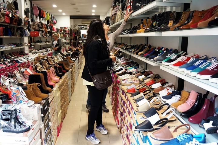 Two women are standing in front of a shoe rack. One woman reaches for something.