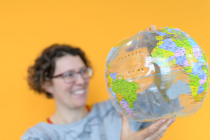 A person is holding a globe in front of an orange wall. 