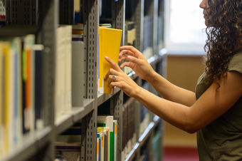 Bild von Studierender in Bibliothek die ein Buch herauszieht